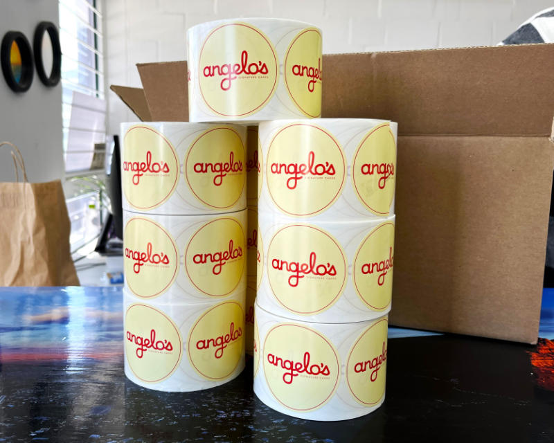 Stacked rolls of round angelo's paper labels in front of a cardboard box