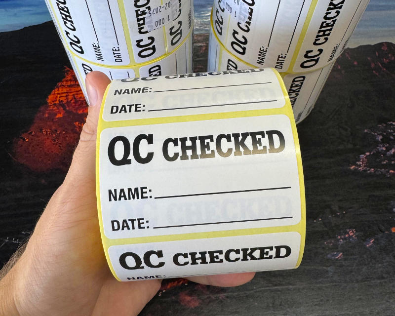 Roll of QC Checked quality control labels with name and date fields, held up close